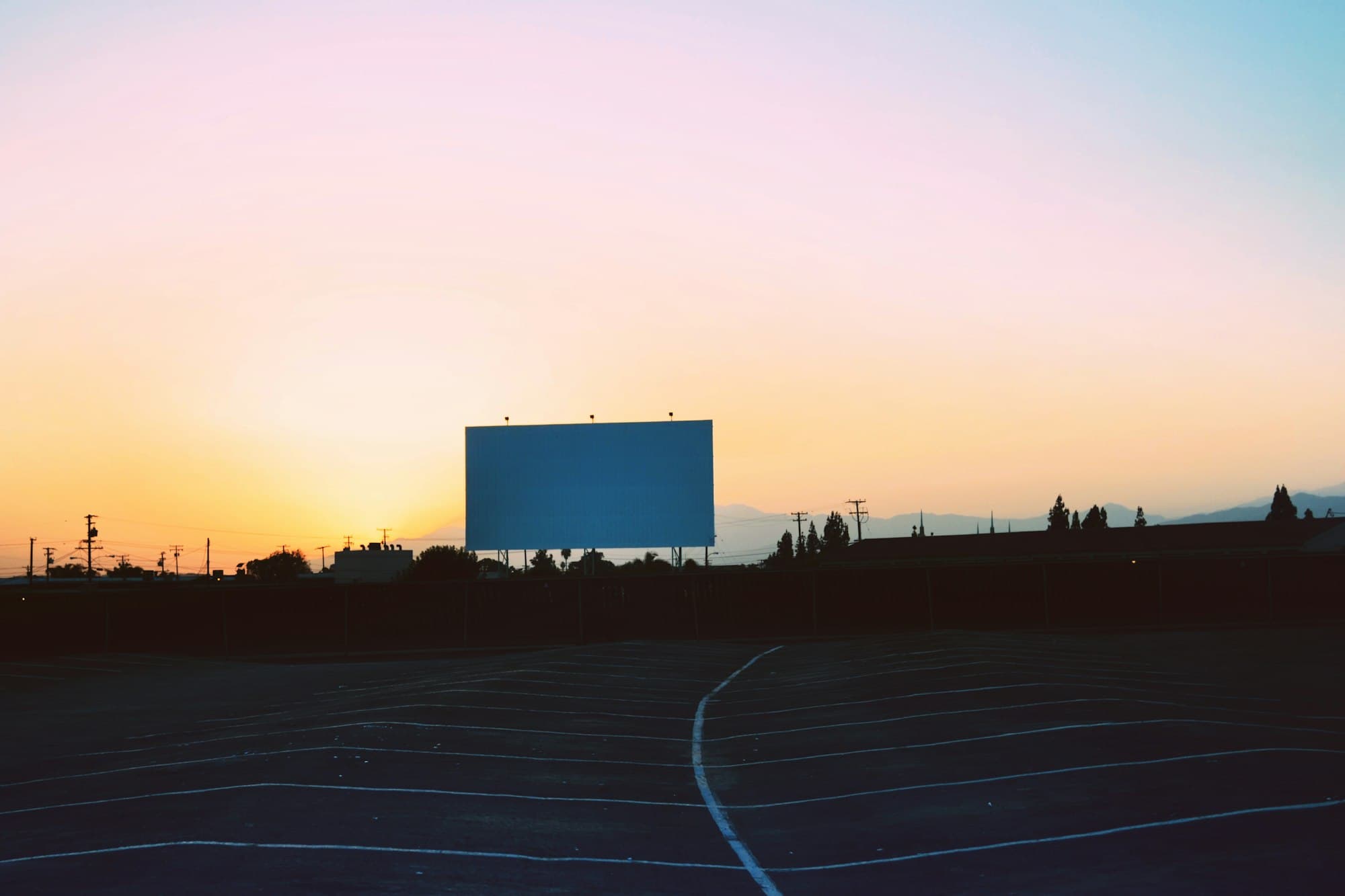 A blank drive-in movie screen above an empty lot under a pastel sunset sky