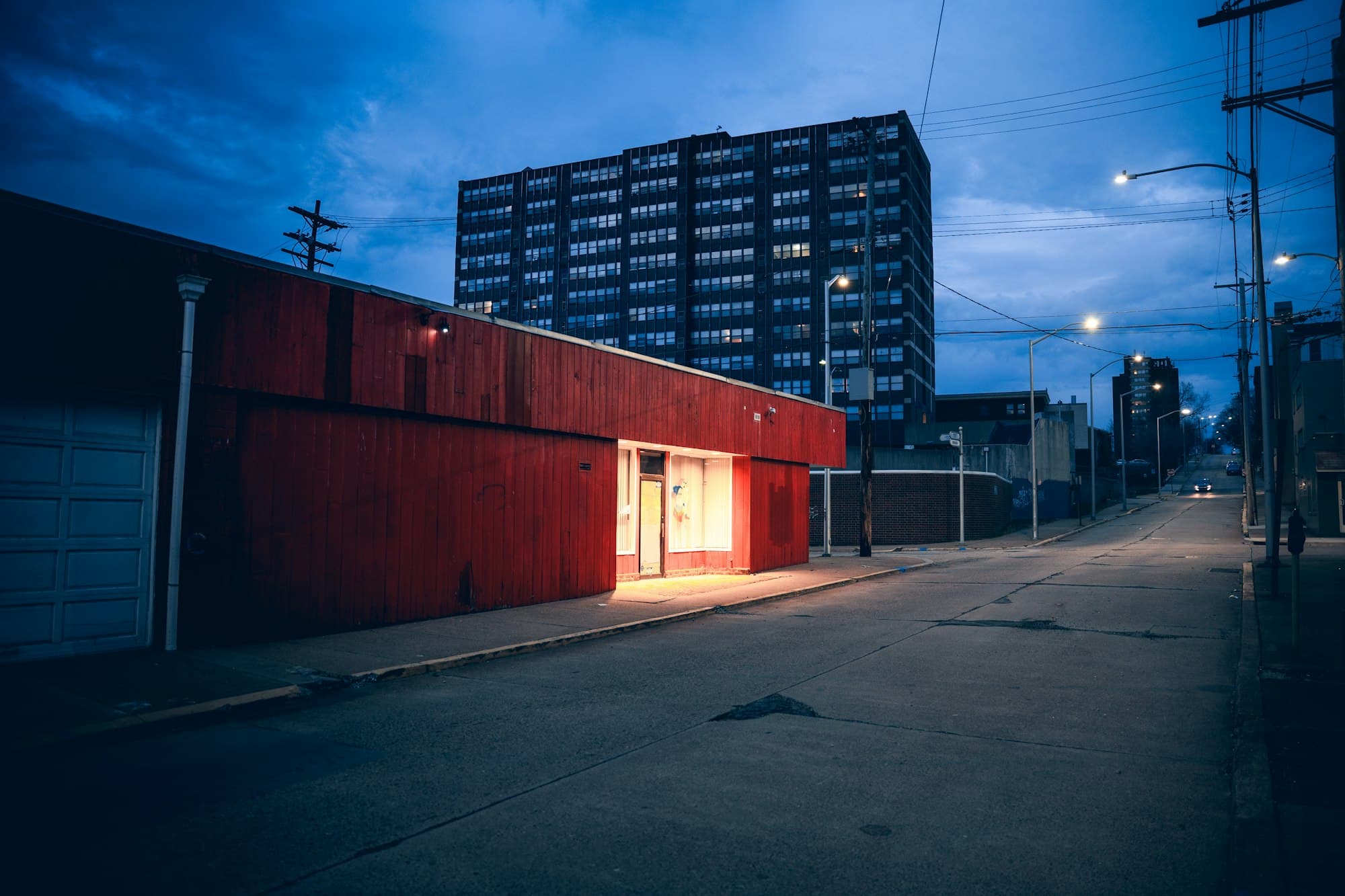 A red building with a lit entrance on an empty city street at dusk