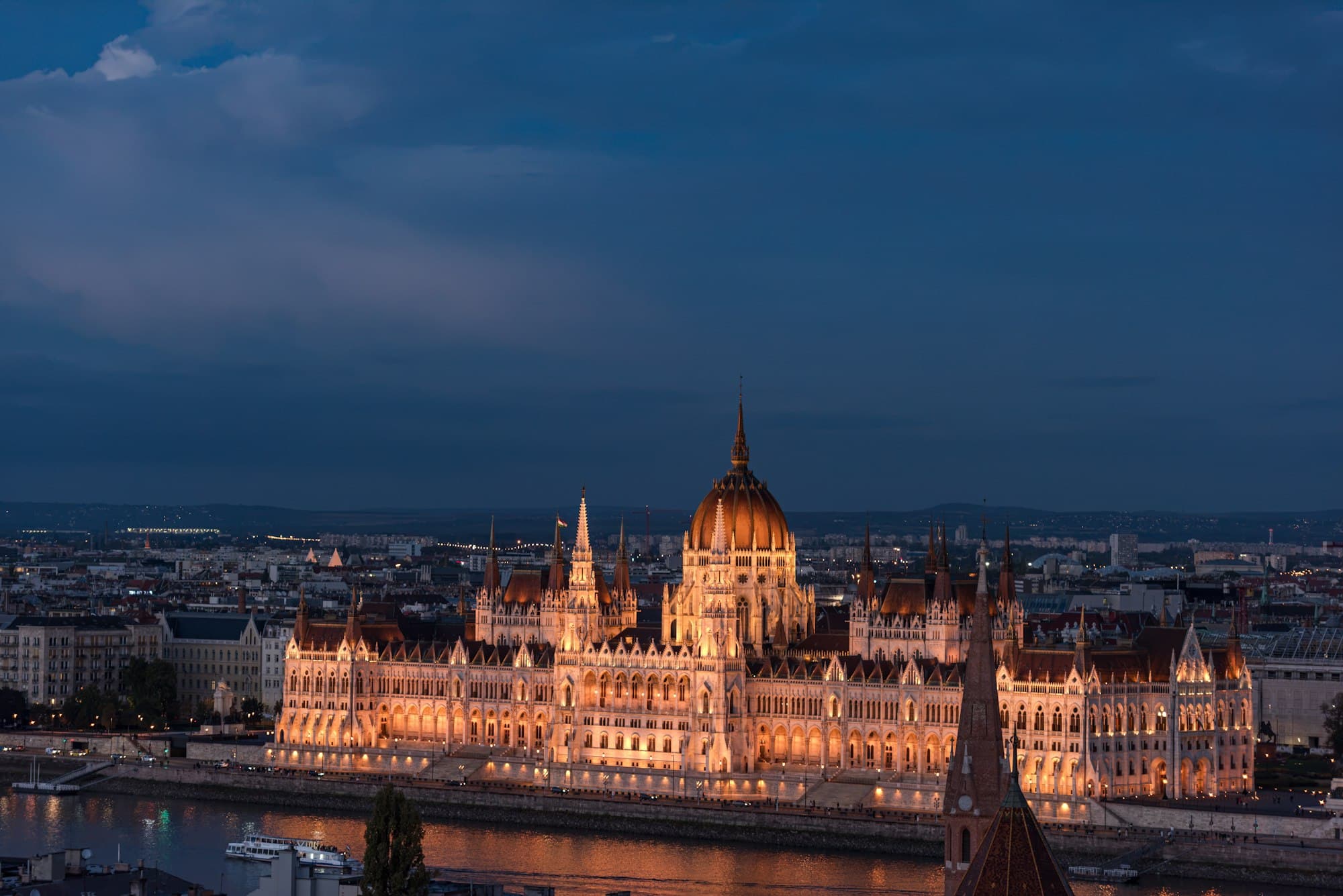 The Hungarian Parliament Building lit up at dusk beside the Danube