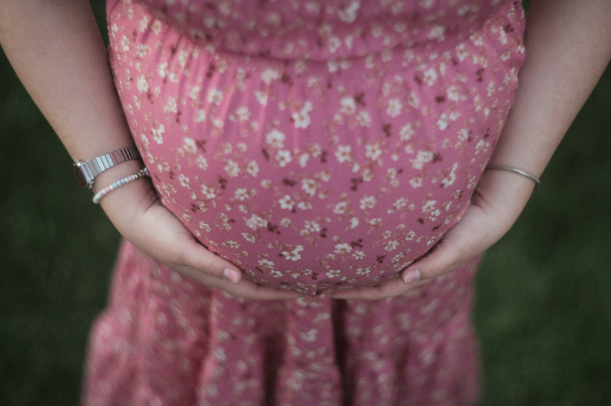 A person in a floral pink dress cradling their pregnant belly with both hands