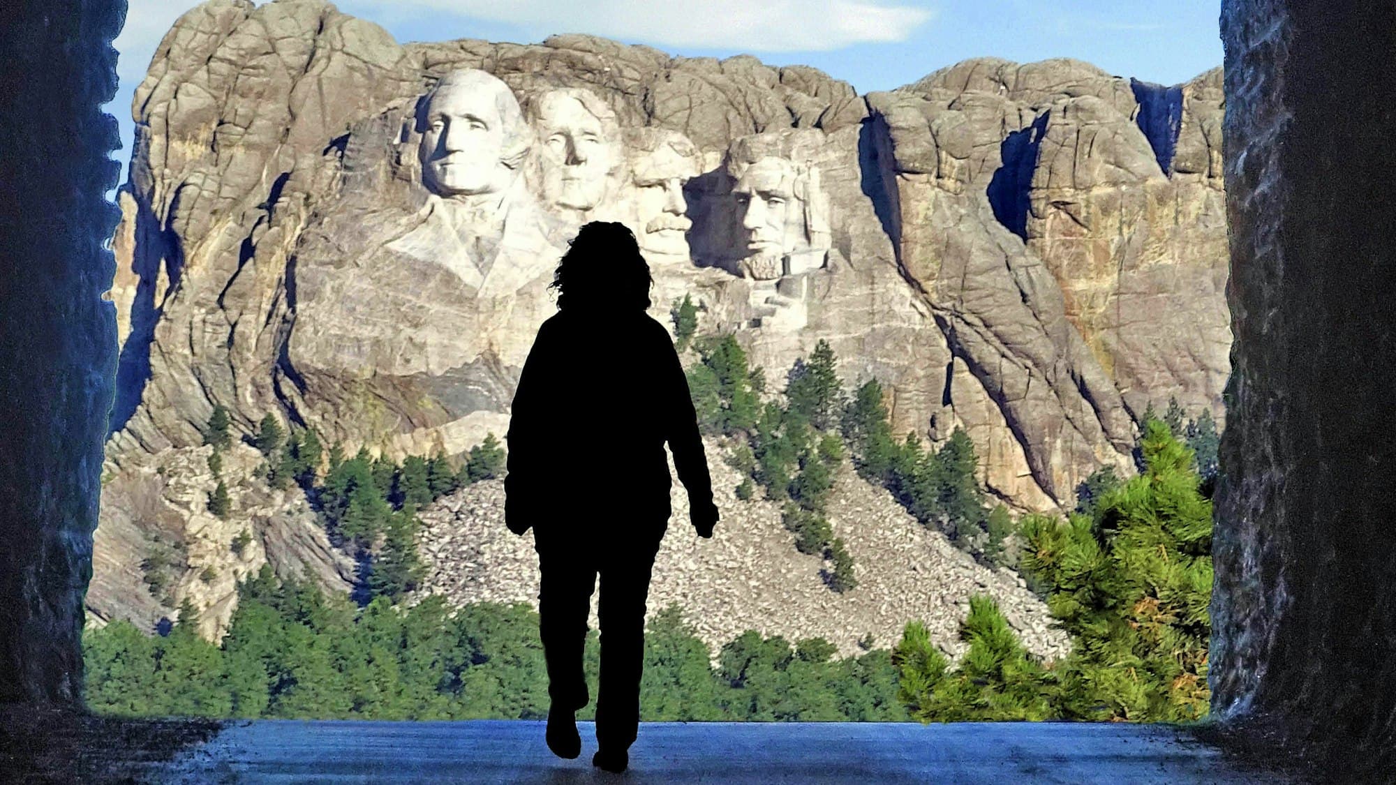 A silhouetted visitor looking out at Mount Rushmore from a rock tunnel