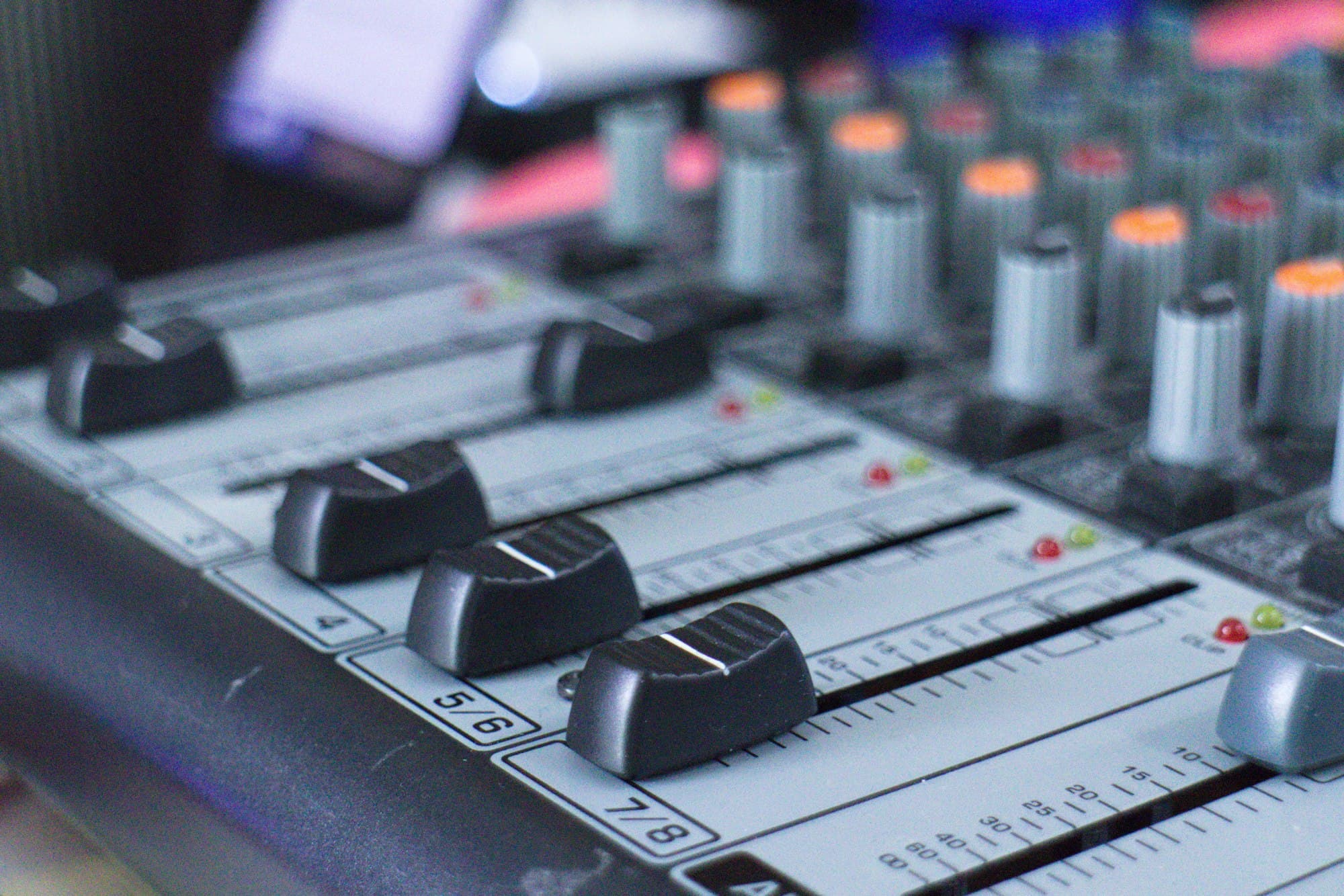 Close-up of an audio mixing console with black faders and colorful knobs
