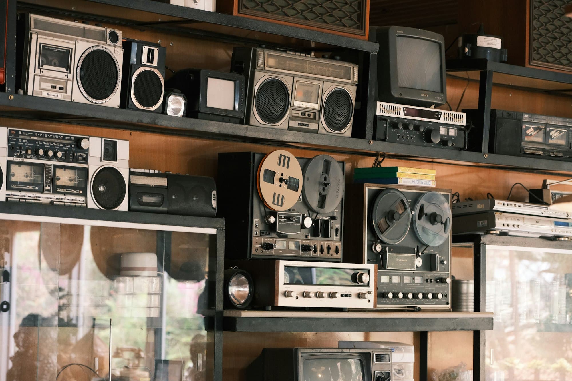 Vintage boomboxes, reel-to-reel tape recorders and old televisions on wooden shelves
