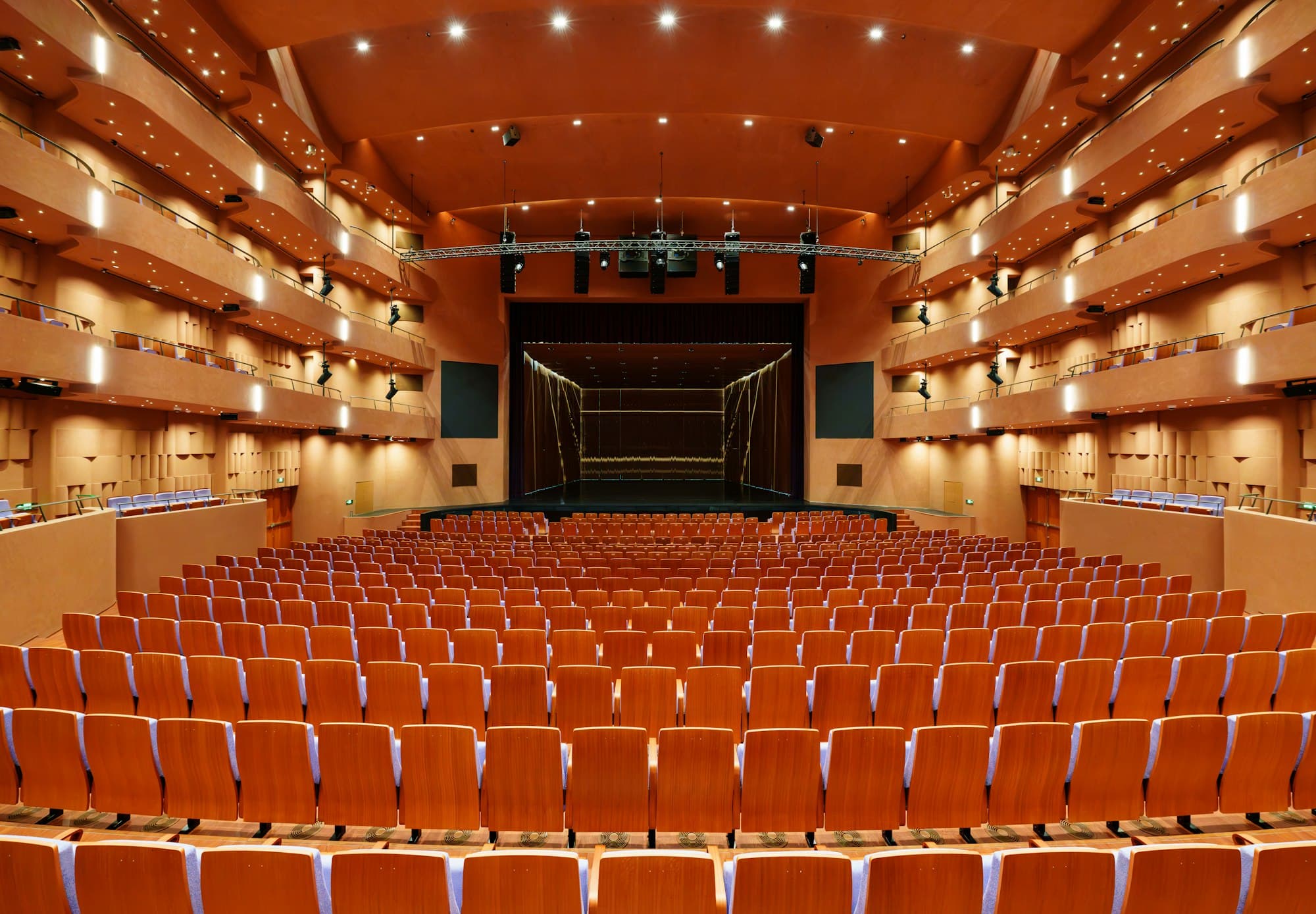 Rows of orange seats facing a stage in a theatre with several balconies
