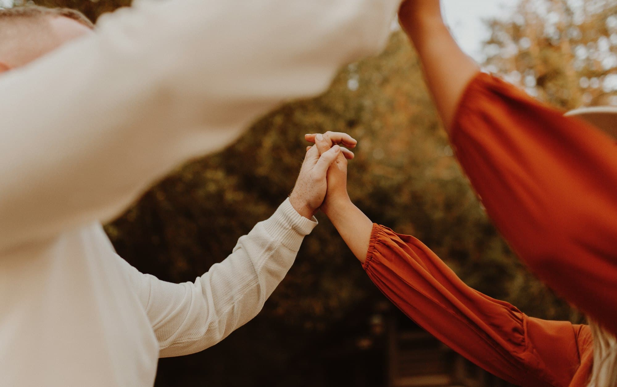 Two people holding hands in a forest at golden hour