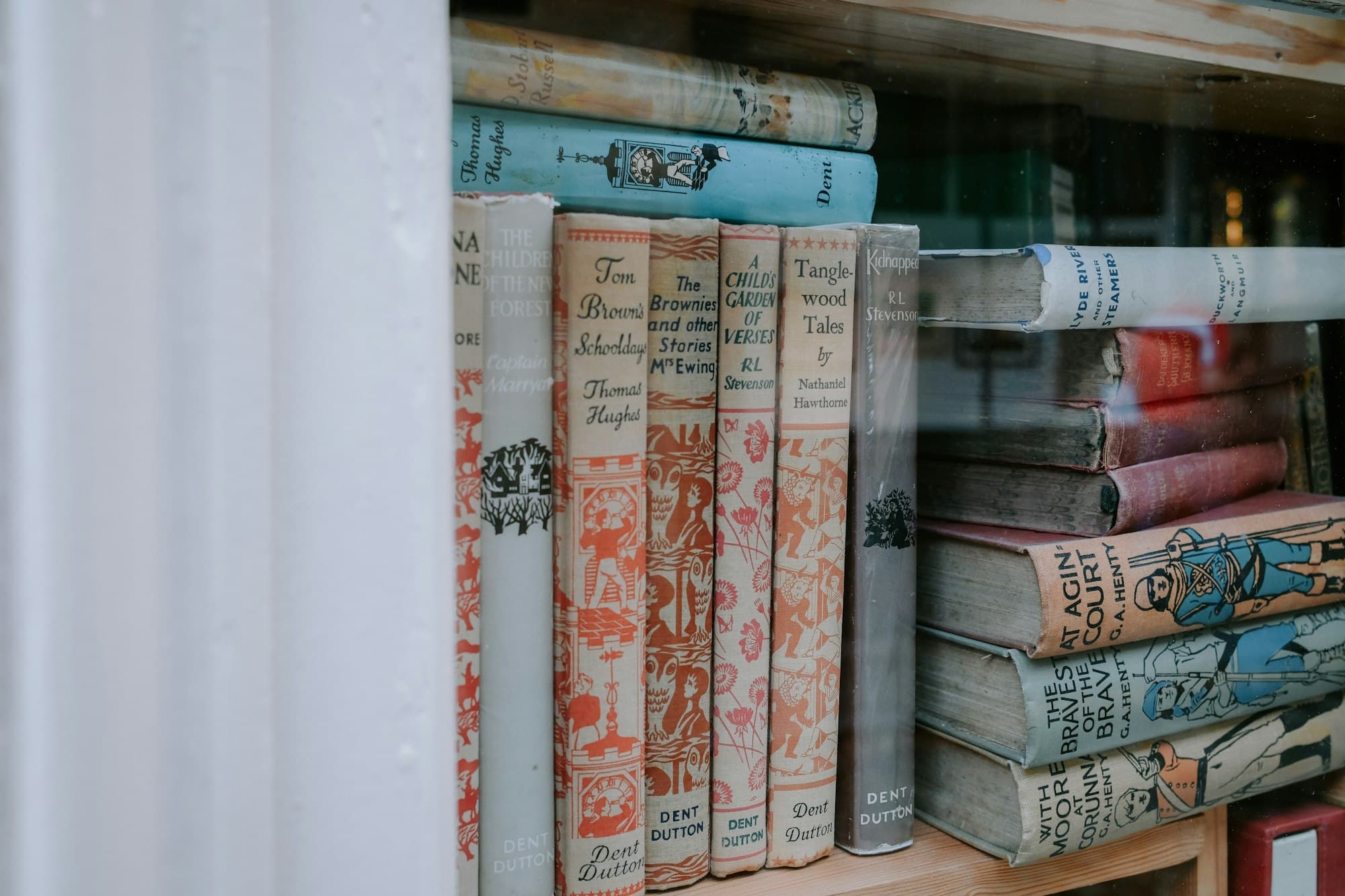 Vintage hardcover storybooks with illustrated spines on a wooden shelf behind glass