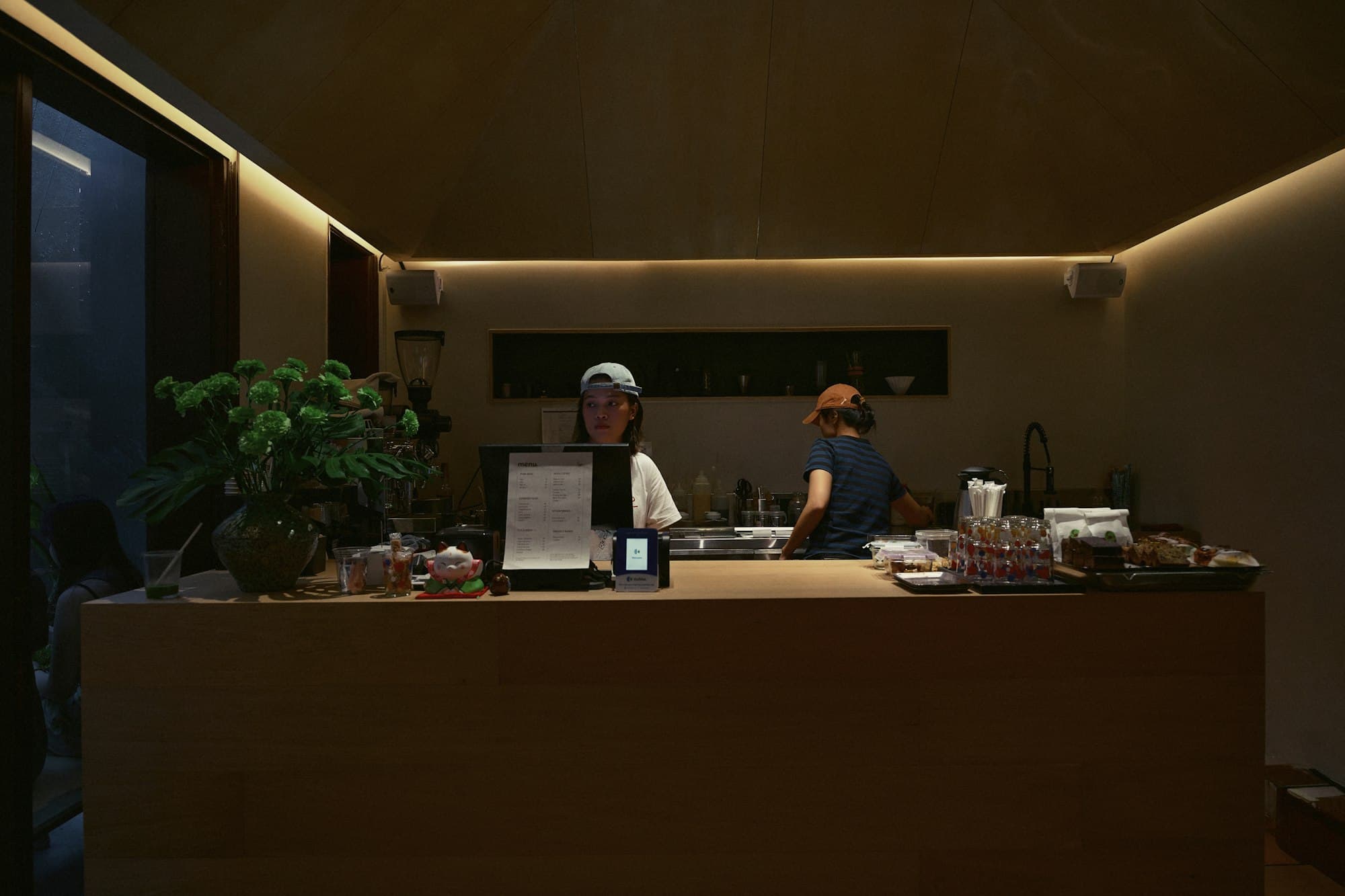 Two people working behind a warm wooden counter in a small coffee shop