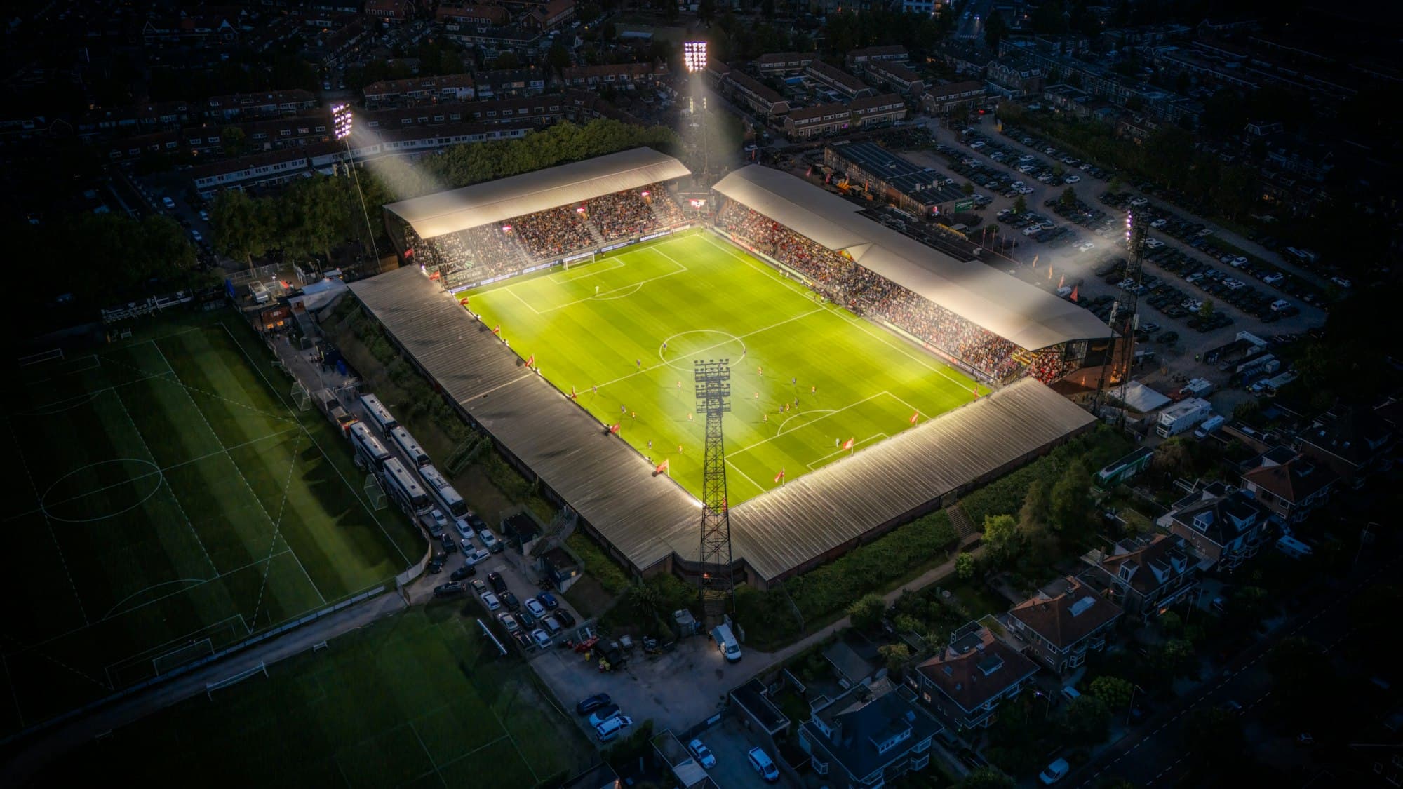 Aerial view of a brightly lit soccer stadium at night surrounded by houses