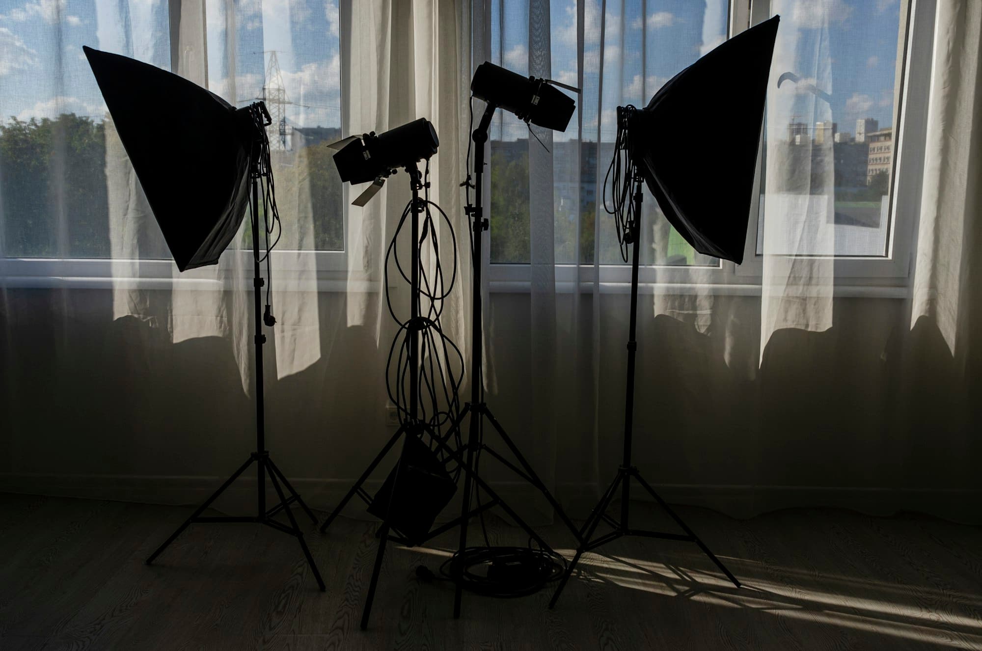 Studio softbox lights on stands silhouetted against a bright curtained window