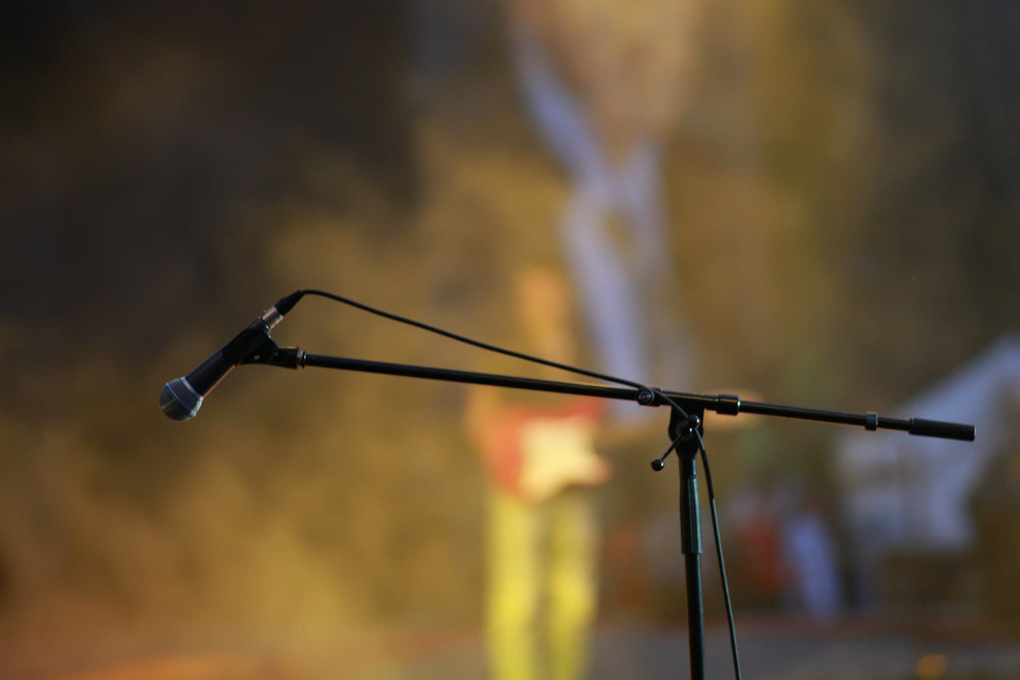 A microphone on a stand against a blurred, warmly lit stage background