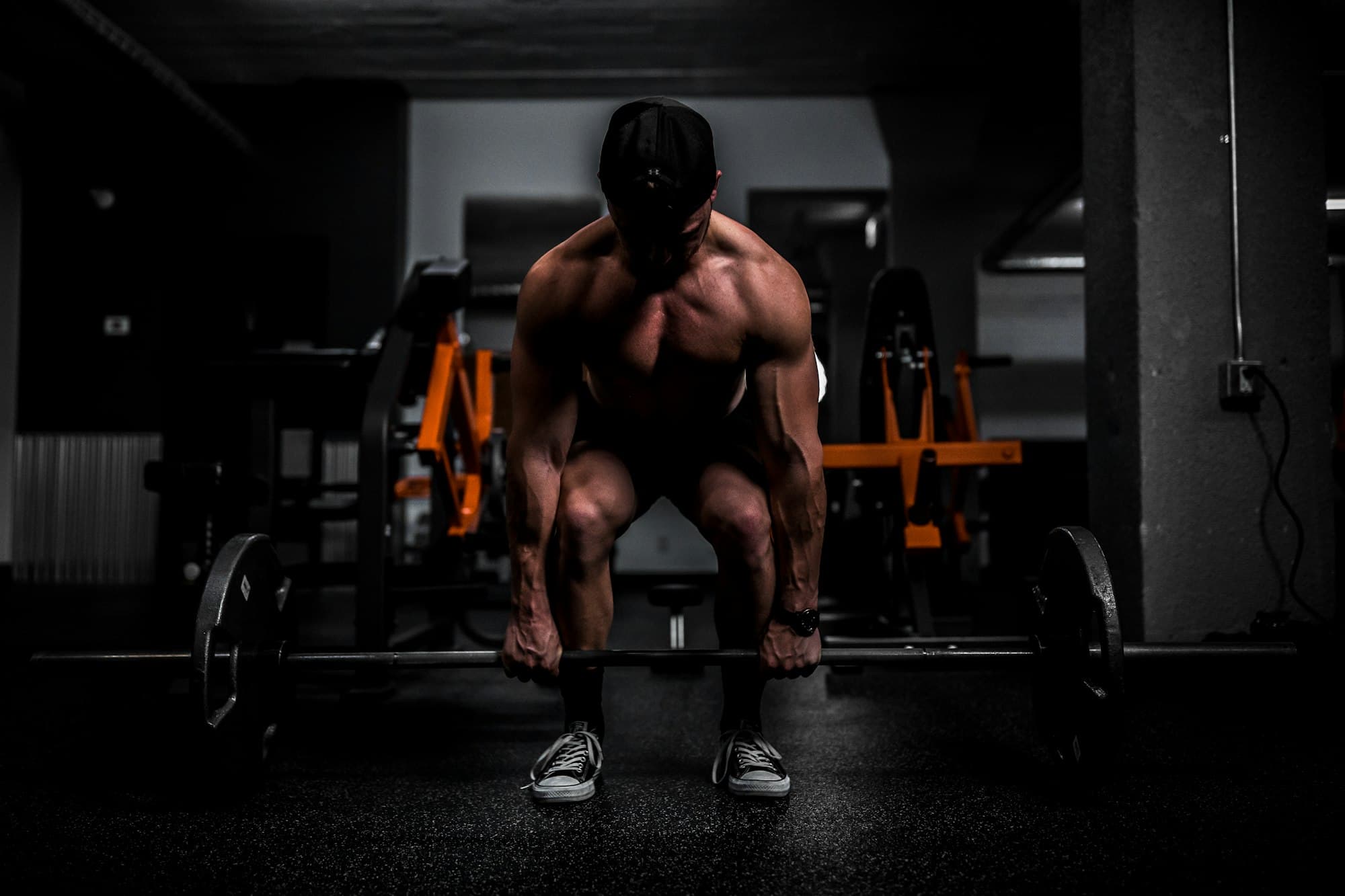 A lifter in a dark gym bent over a loaded barbell, about to deadlift
