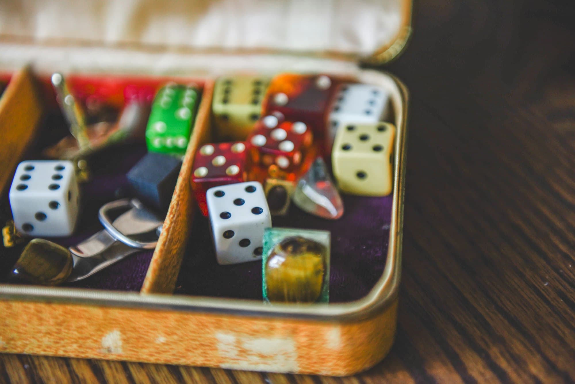 An old tin box lined with purple velvet holds a jumble of colourful gaming dice and small trinkets
