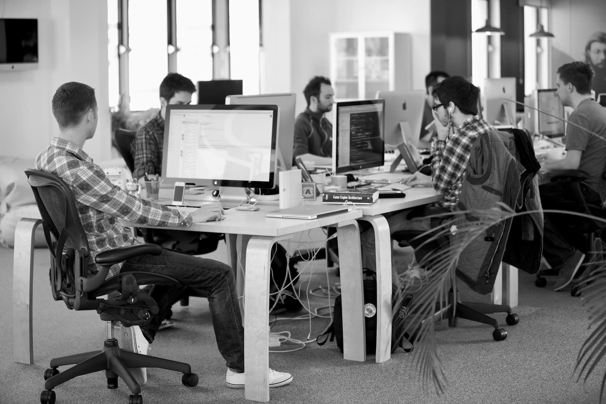 Developers working at computers around a shared desk in a black and white open office