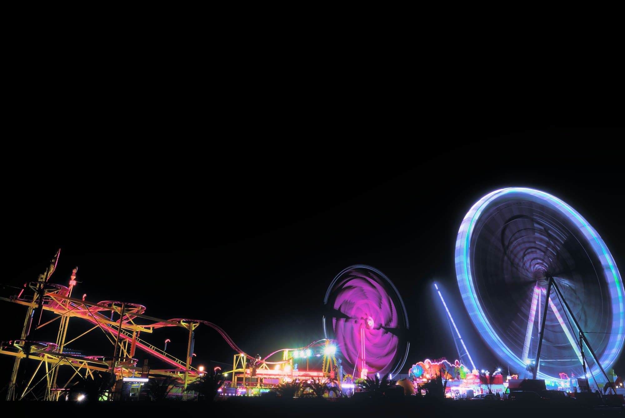 A long exposure of a roller coaster and ferris wheel lit up at night