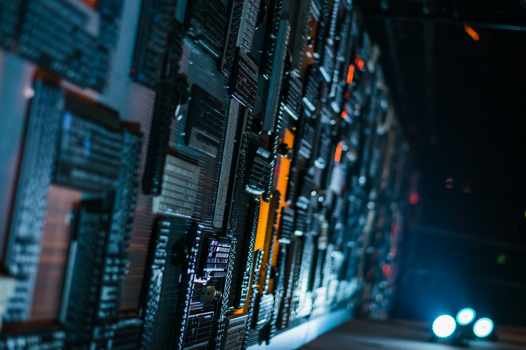 A dark corridor lined with a wall of circuit boards and drives under teal lights