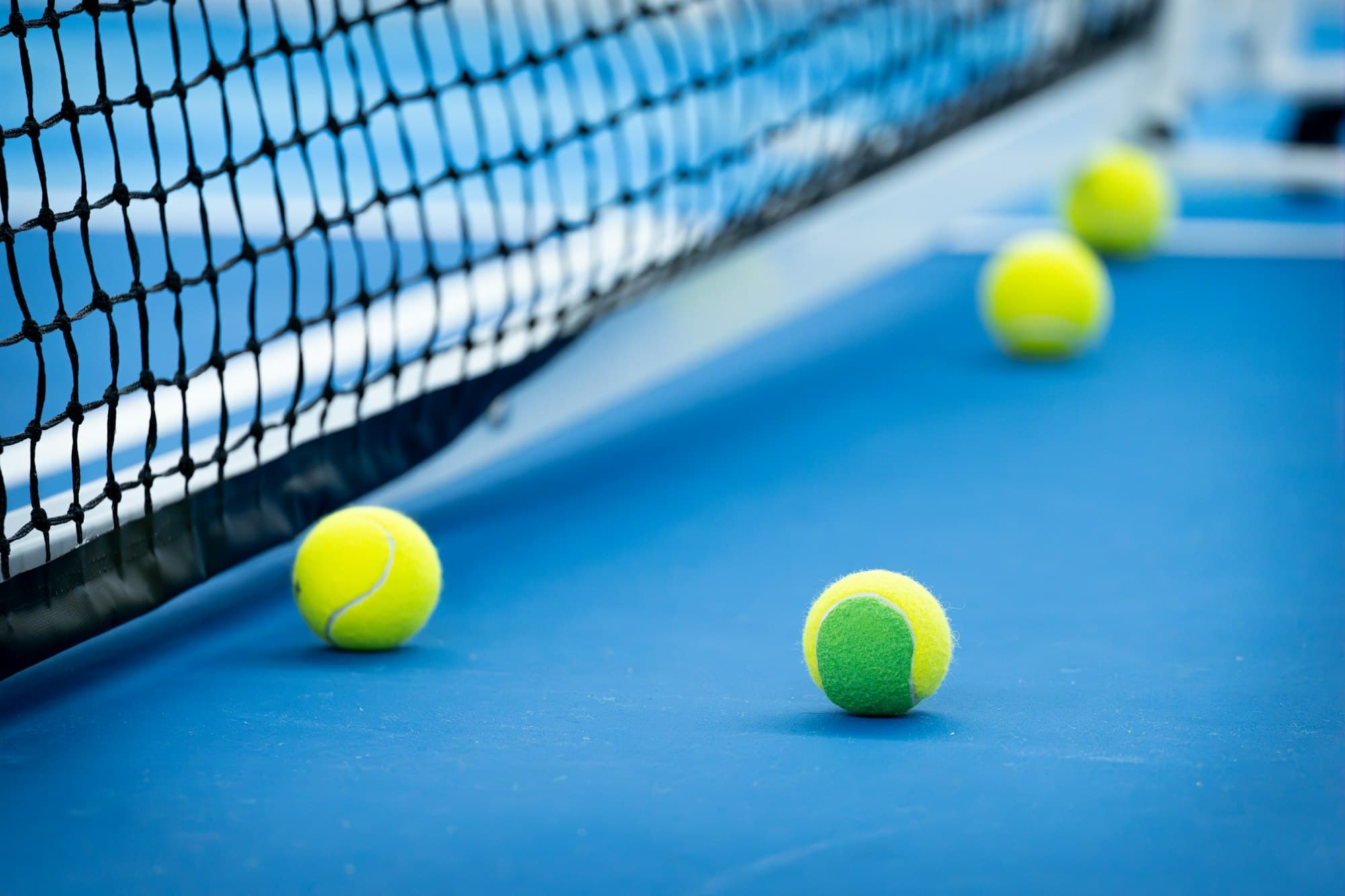 Yellow tennis balls on a blue hard court beside the net