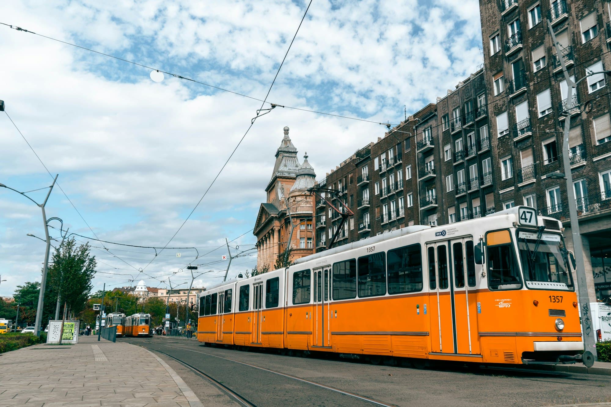 A yellow and white tram on tracks in Budapest beside historic buildings
