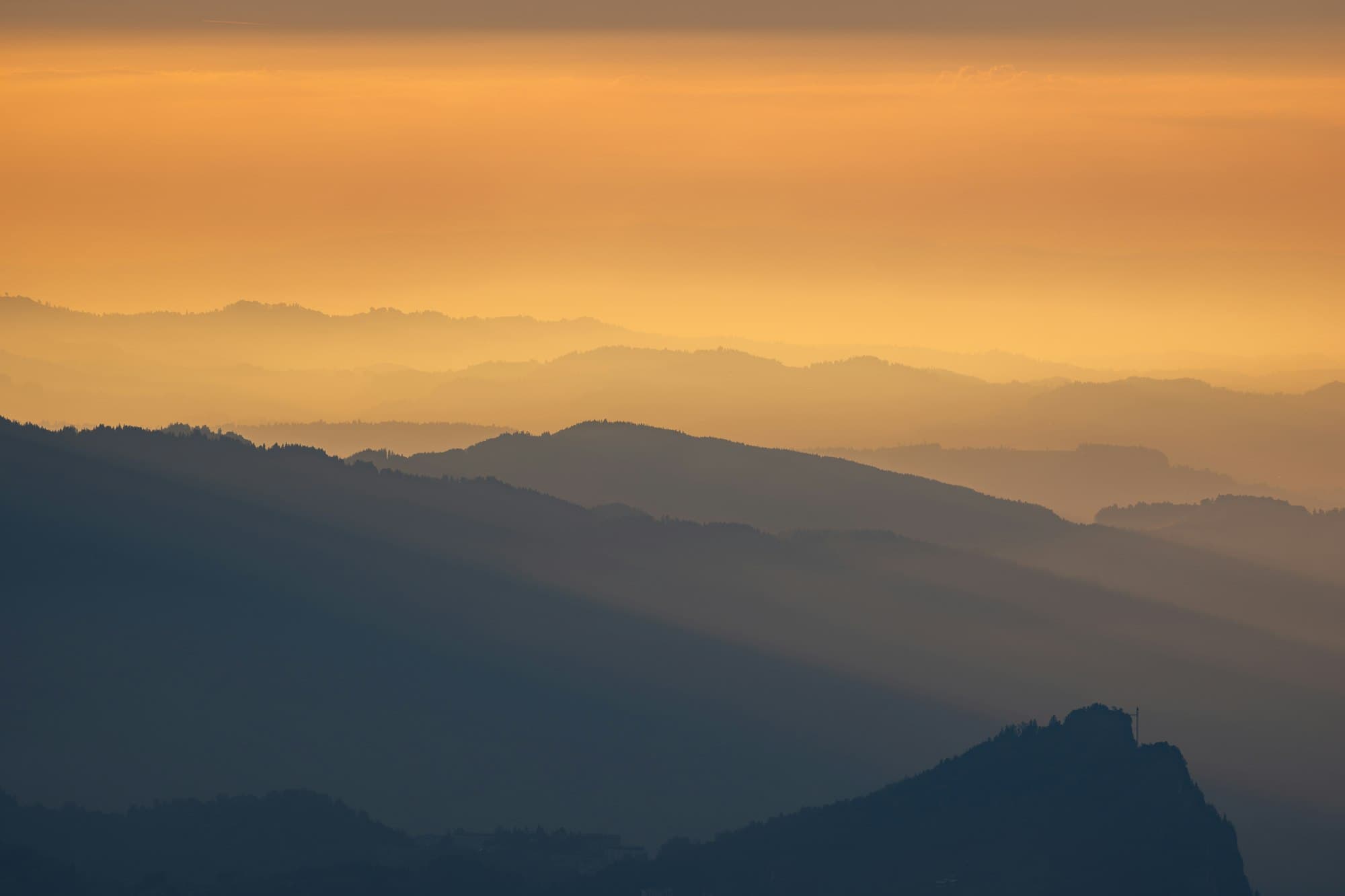 Layered mountain ridges fading into a warm orange sky at golden hour