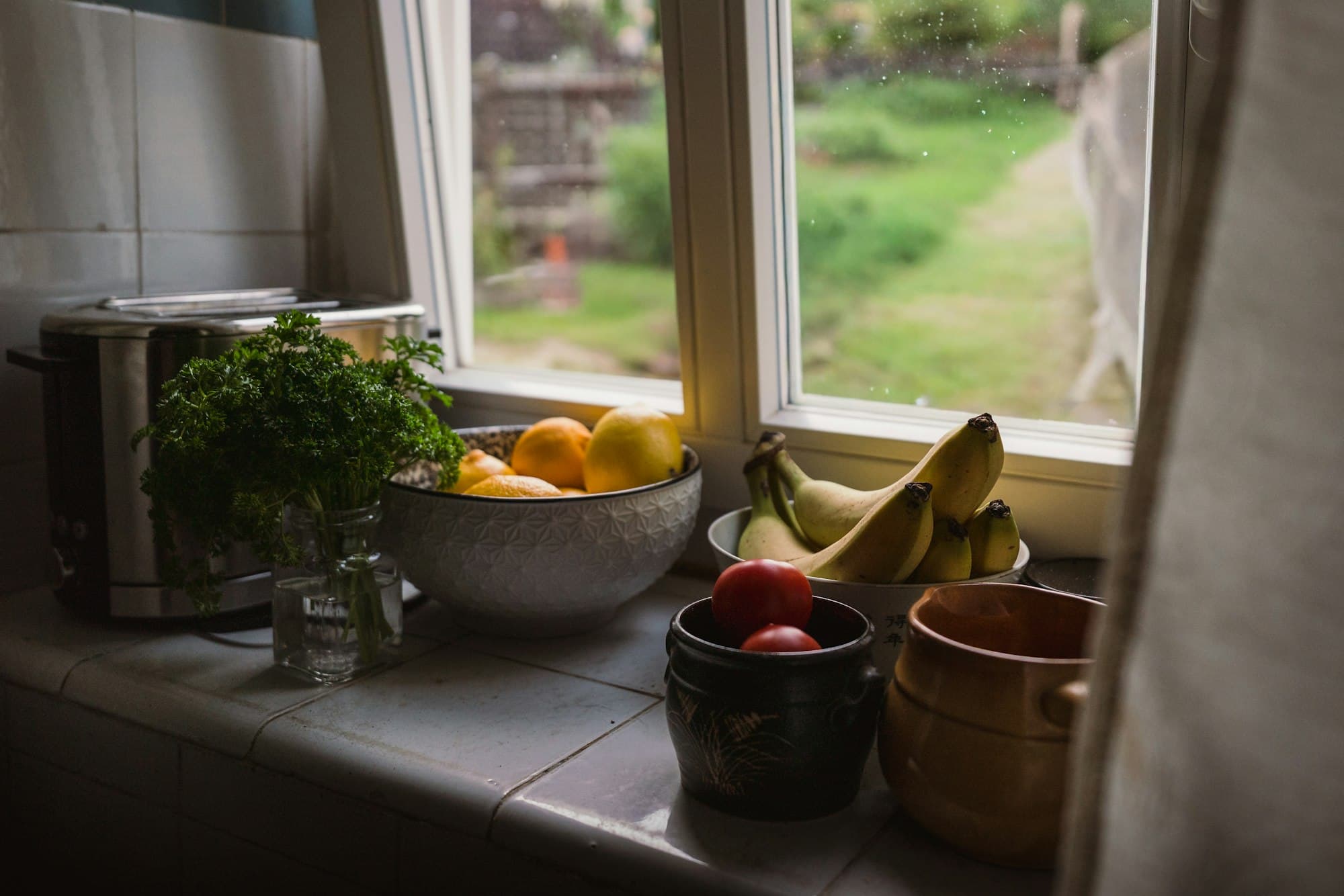 Lemons, bananas, tomatoes and parsley on a kitchen windowsill beside an open window