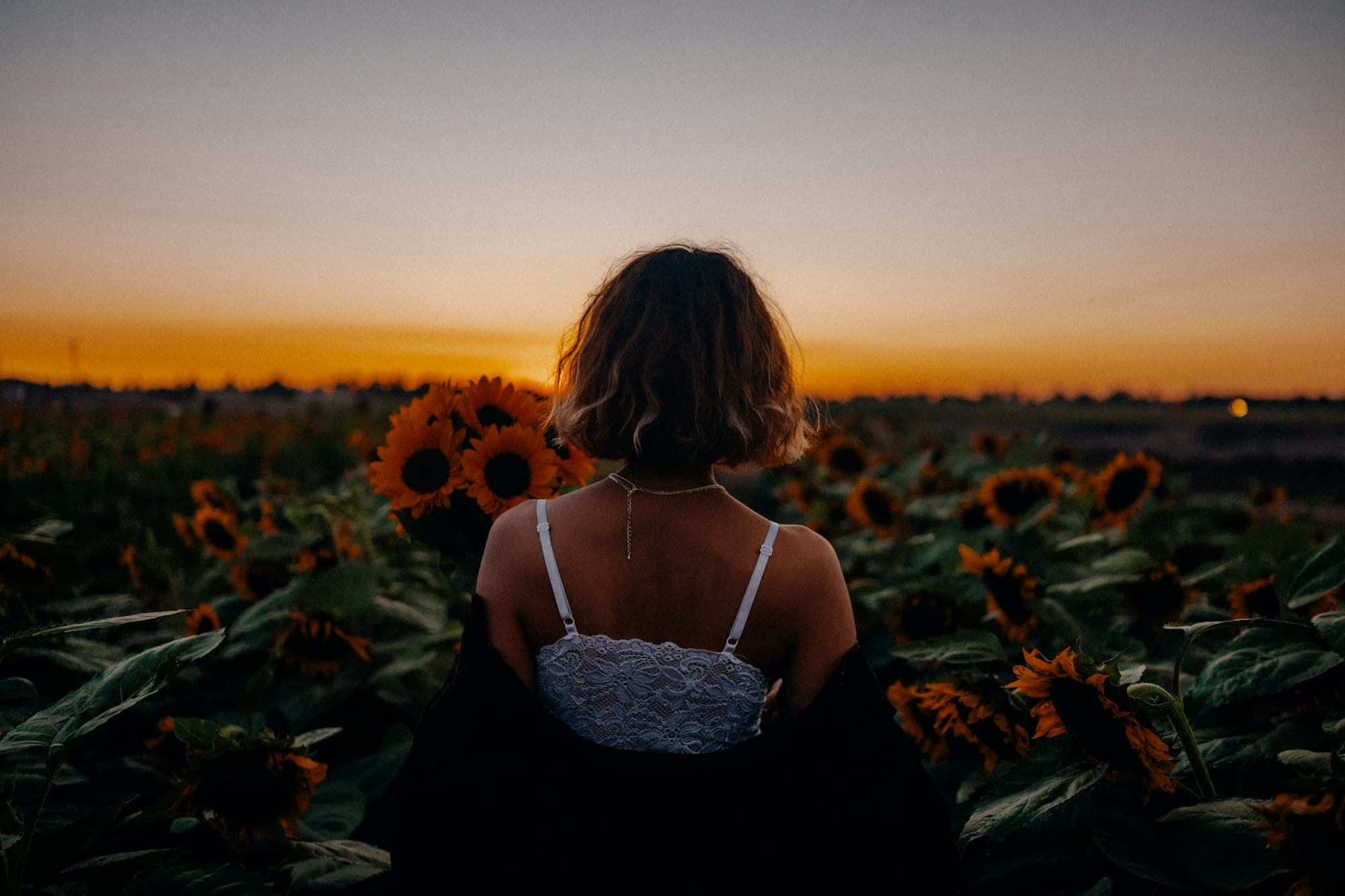 A woman seen from behind in a sunflower field at sunset