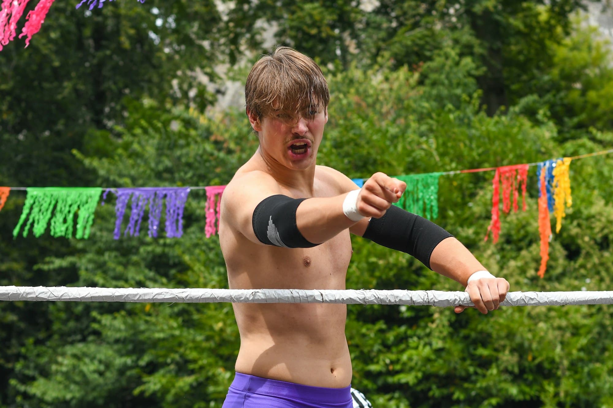 A wrestler pointing forward from inside a ring with ropes and colourful bunting